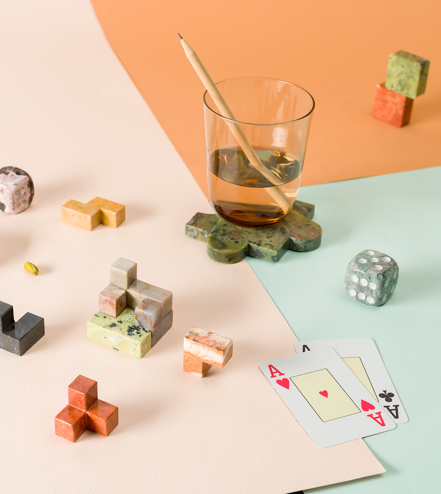 Colorful stone puzzle pieces, a glass with a straw, and playing cards on a pastel background