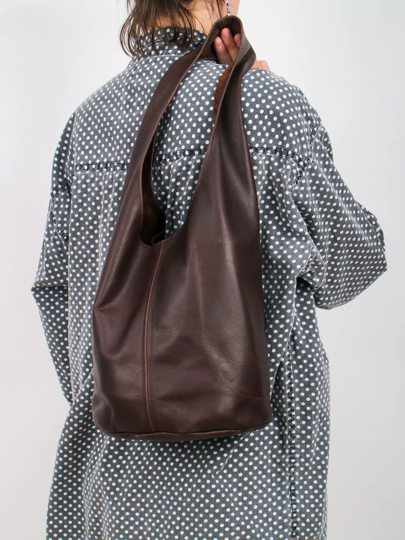 Person with a polka dot shirt wearing a dark brown leather bag over one shoulder against a plain background