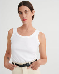 Woman wearing a white tank top and beige pants against a plain background