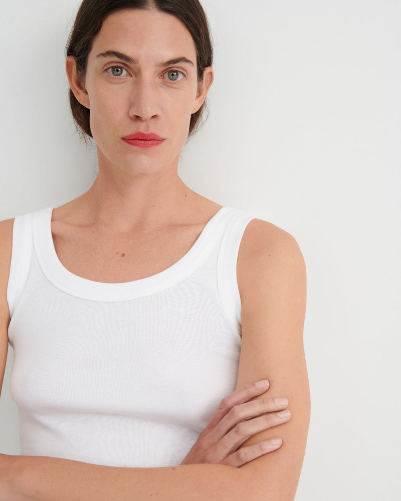 Woman wearing a white tank top against a plain background