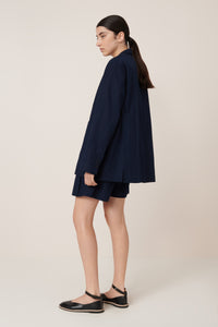 Woman wearing a navy blue outfit with a jacket and shorts on a beige background