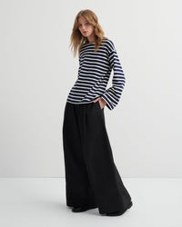 Woman wearing a navy and white striped top and black wide-leg pants on a white background