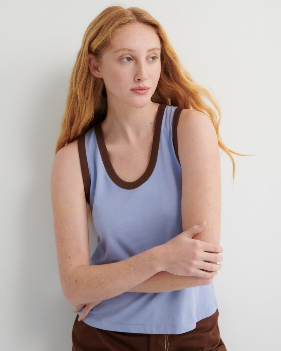 Woman wearing a light blue tank top with brown trim against a plain background
