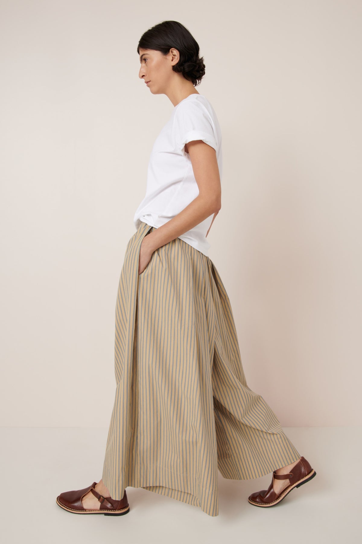 Person wearing a white t-shirt and beige striped pants on a plain background