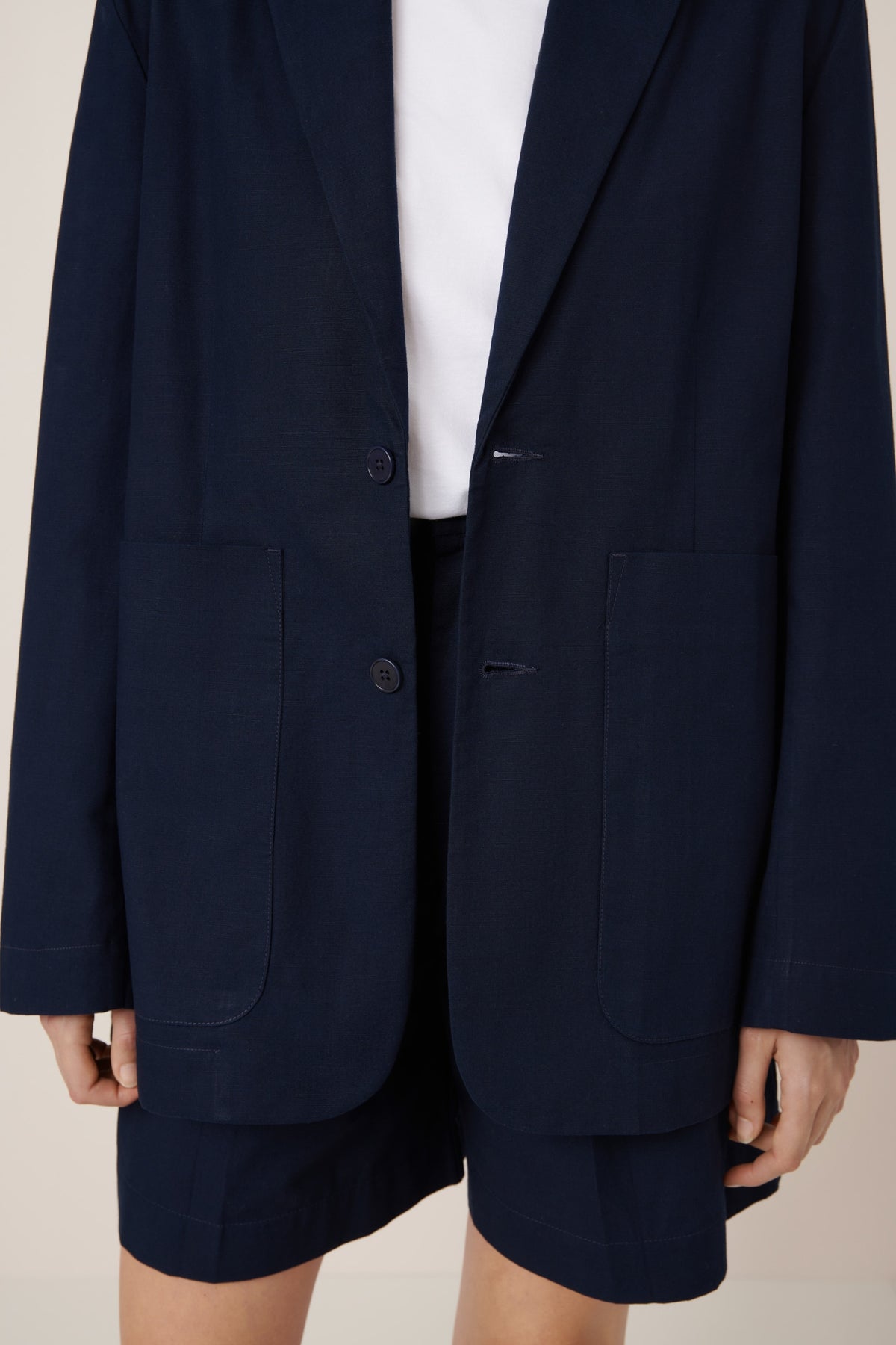 Navy blazer worn open over a white shirt and shorts on a neutral background
