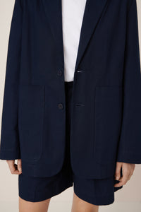 Navy blazer worn open over a white shirt and shorts on a neutral background