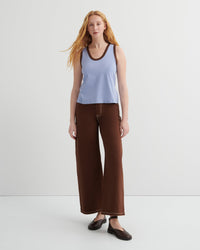 Woman wearing a light blue tank top and brown wide-leg pants on a white background