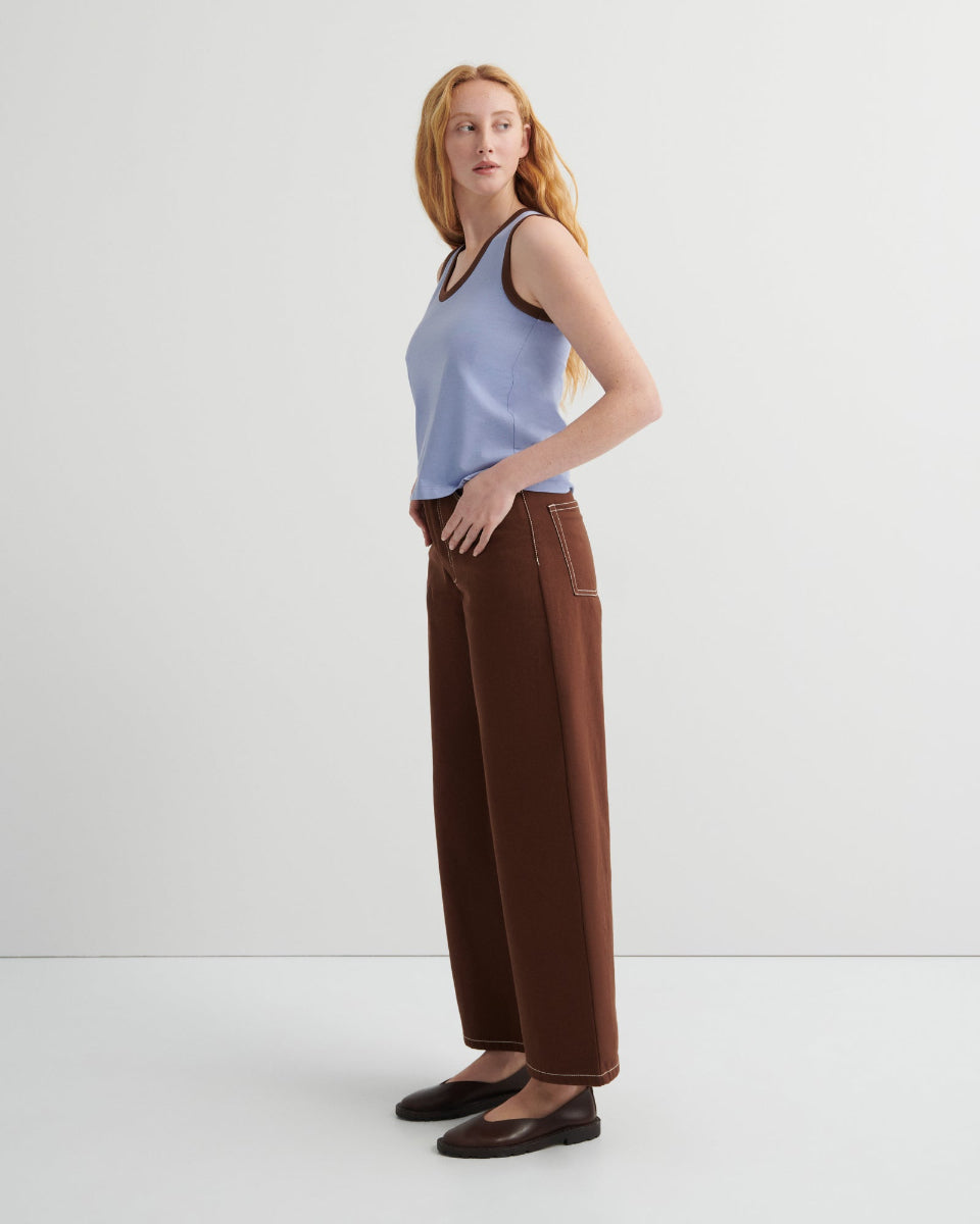 Woman wearing a light blue sleeveless top and brown pants on a white background