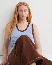 Woman wearing a light blue tank top and brown pants against a white background