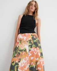 Woman wearing a black top and colorful floral skirt against a white background