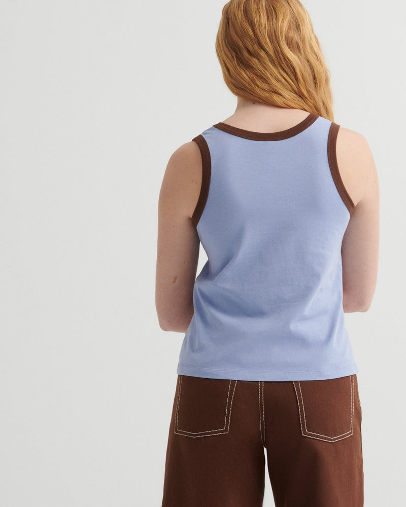 Person wearing a light blue tank top and brown pants on a plain background