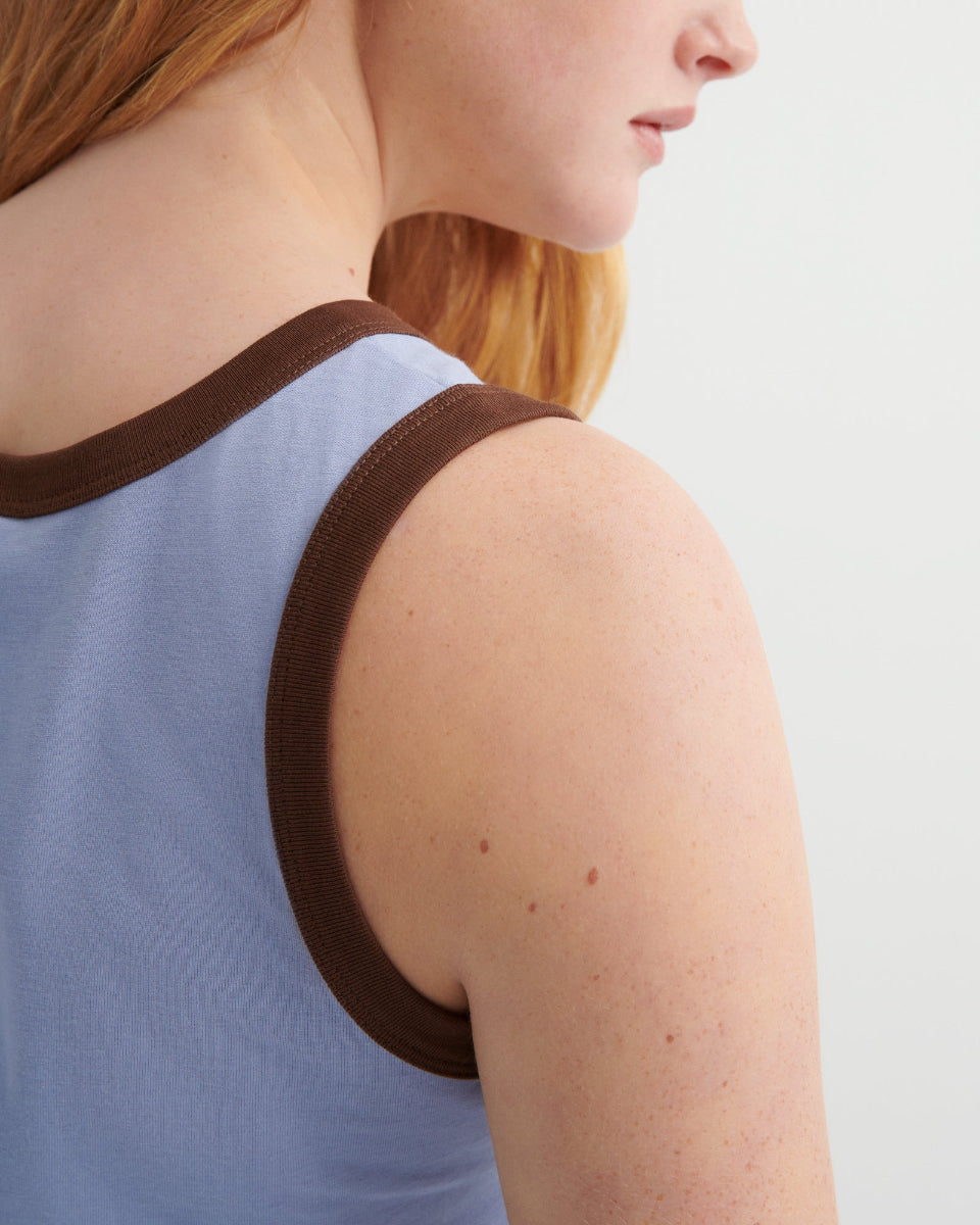 Person wearing a blue tank top with brown trim on a light gray background