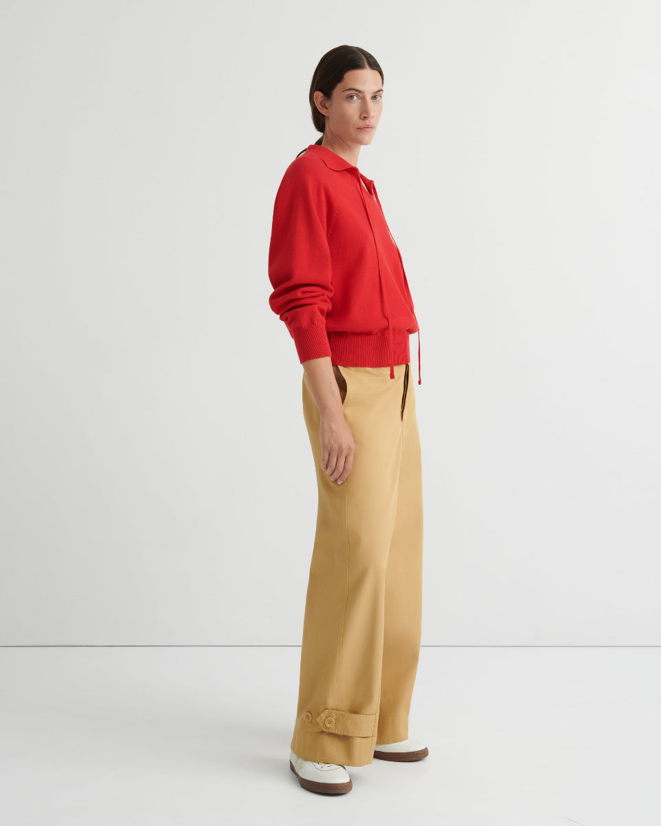 Person wearing a red collared sweater and tan pants on a white background