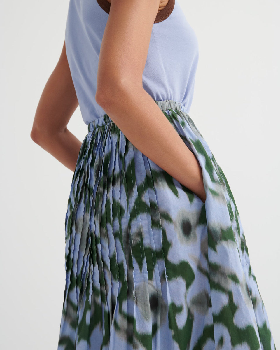 Person wearing a light blue top and green floral skirt on a white background
