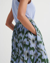 Person wearing a light blue top and green floral skirt on a white background