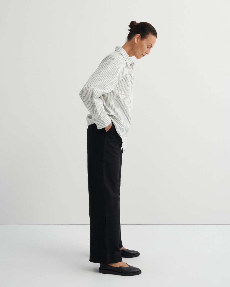 Person wearing a striped shirt and black pants on a white background
