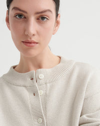 Person wearing a light beige cardigan on a plain background