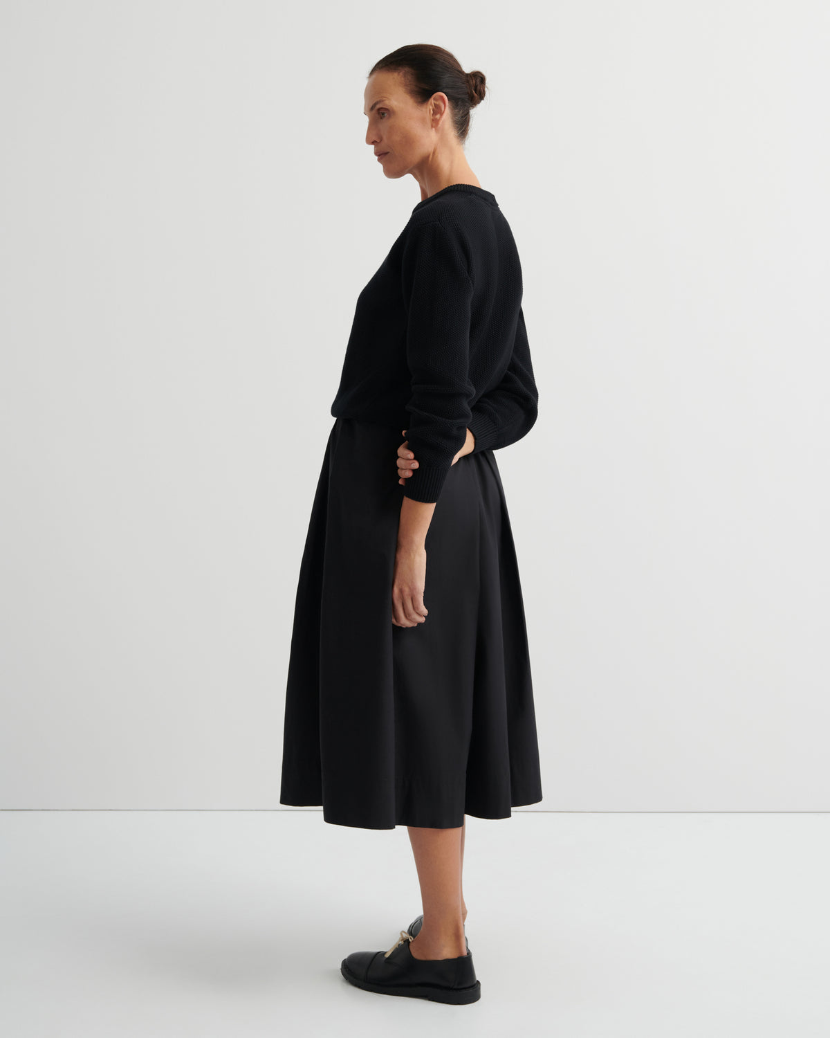 Woman wearing a black sweater and culottes against a white background