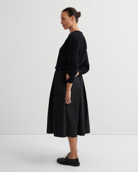 Woman wearing a black sweater and culottes against a white background