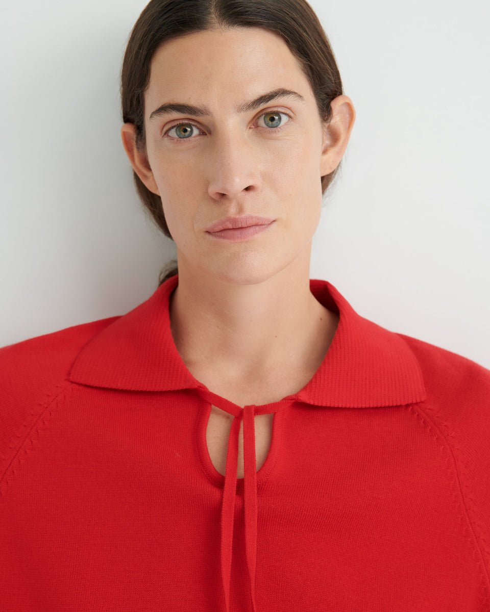 Person wearing a collared red knit top on a white background