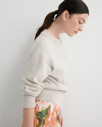 Woman wearing a light beige sweater with a floral skirt against a plain background
