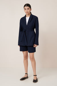 Person wearing a navy blue blazer and shorts set on a beige background