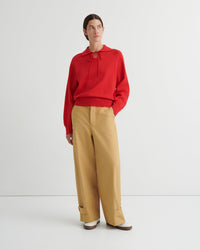 Person wearing a red collared sweater and tan pants on a white background