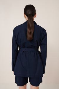 Person wearing a navy blue belted coat and shorts on a beige background