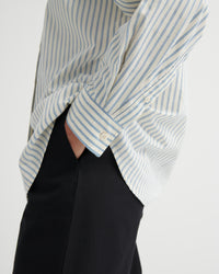 Close-up of a person wearing a striped shirt and black pants on a light gray background