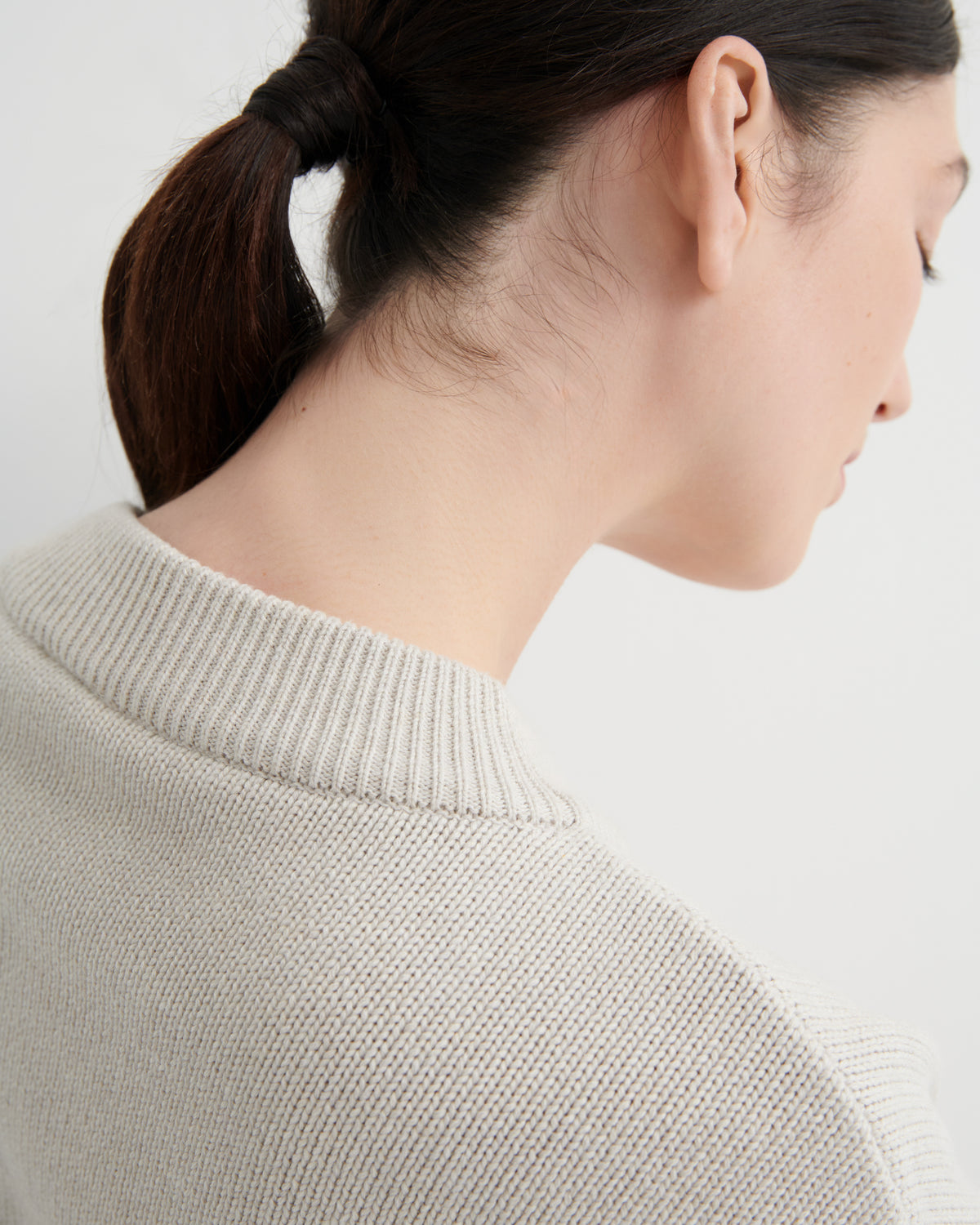 Close-up of a person wearing a light beige sweater on a plain background
