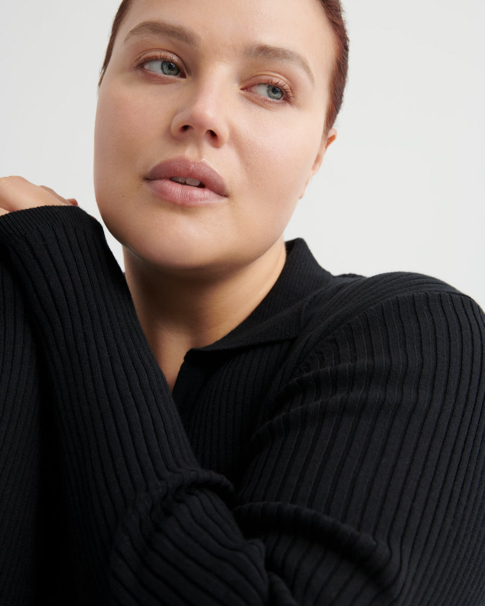 Person wearing a black ribbed sweater against a light background