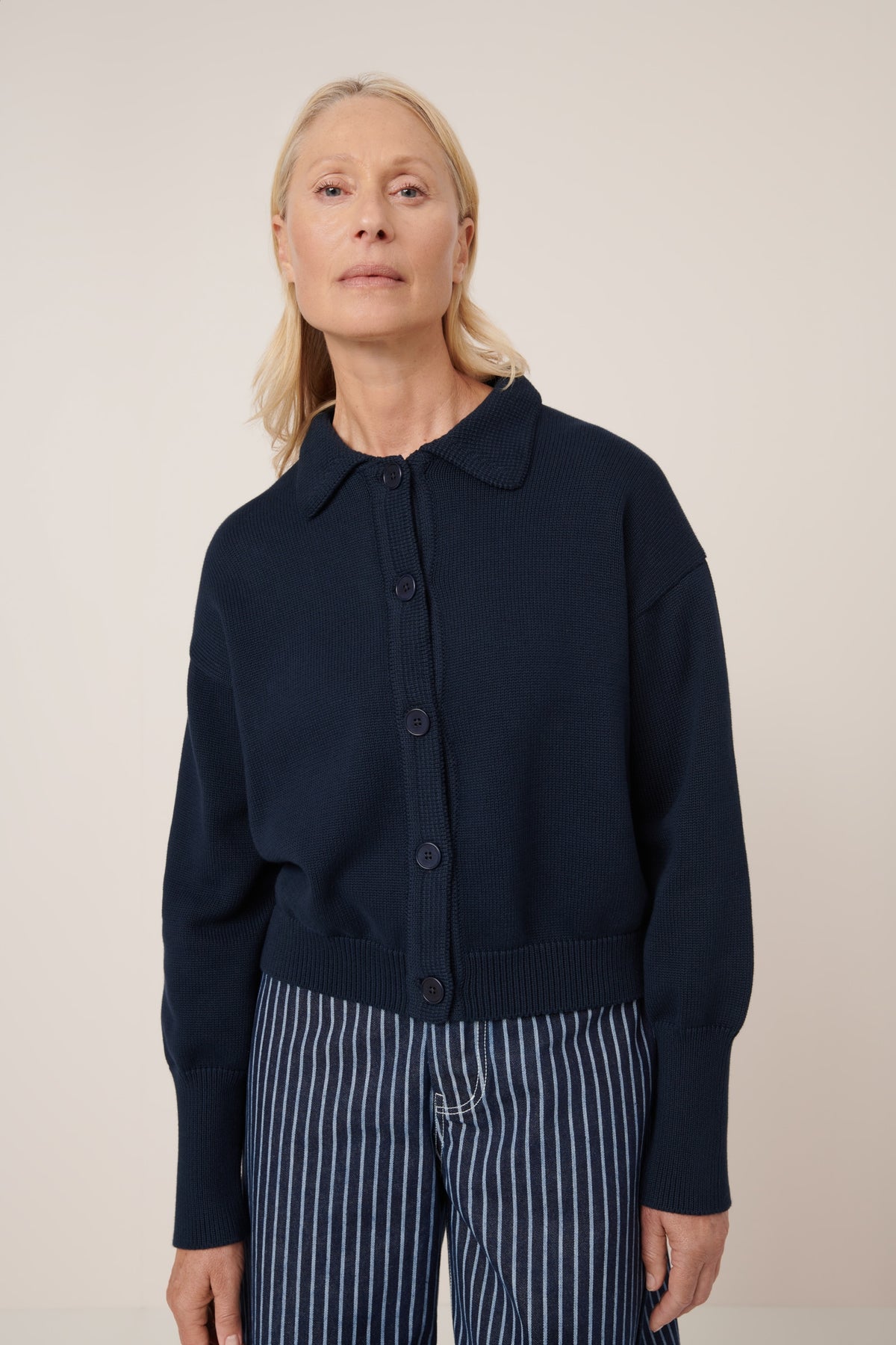 Woman wearing a navy blue cardigan with striped pants on a beige background