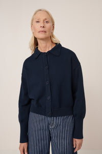 Woman wearing a navy blue cardigan with striped pants on a beige background