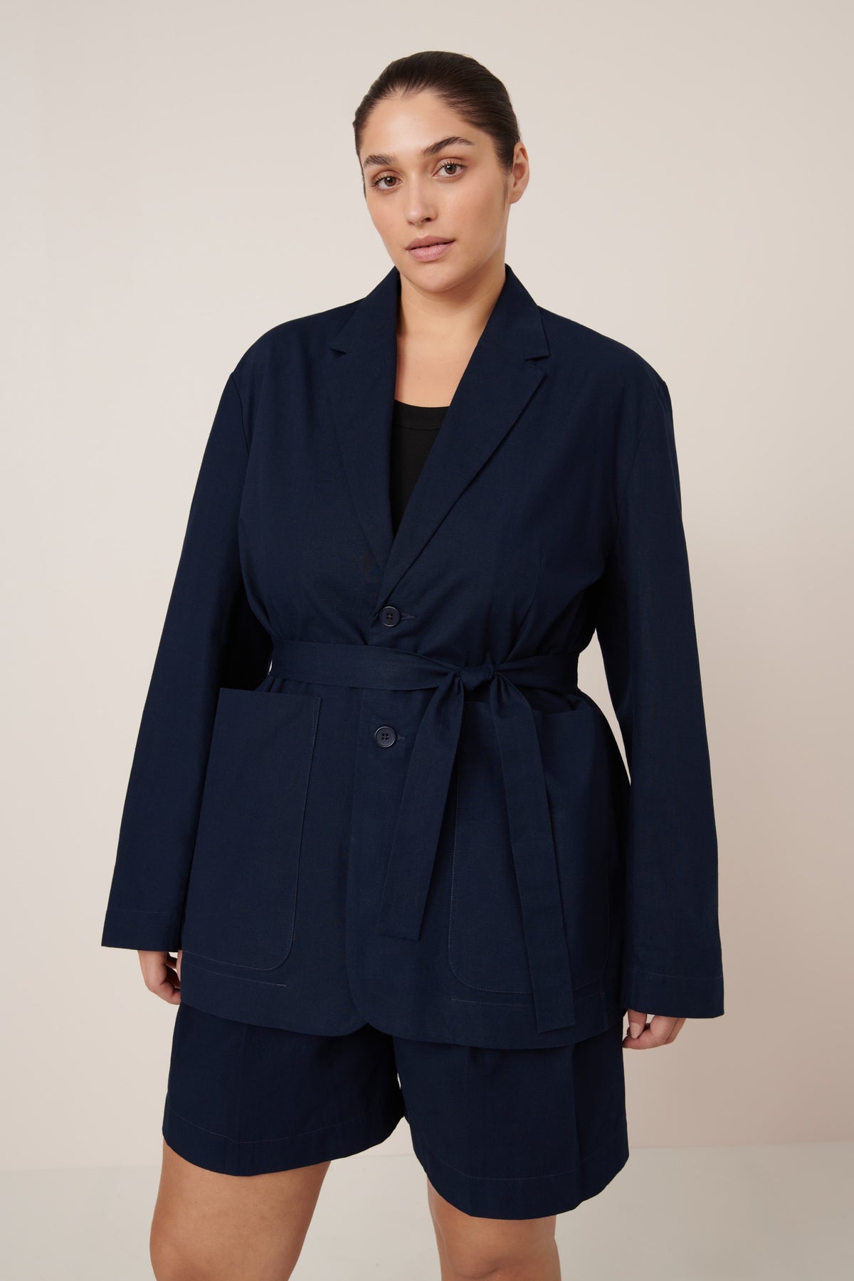 Woman wearing a navy blue blazer and shorts set on a beige background