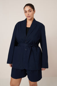 Woman wearing a navy blue blazer and shorts set on a beige background