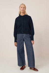 Person wearing a navy cardigan and striped pants on a white background