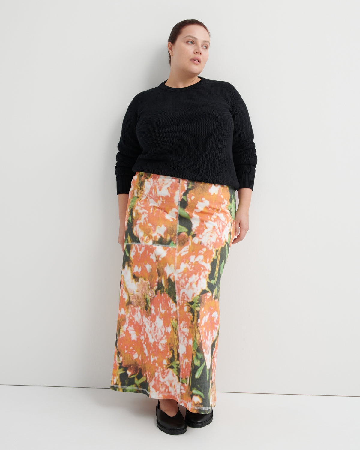 Woman wearing a black sweater and floral skirt against a white background