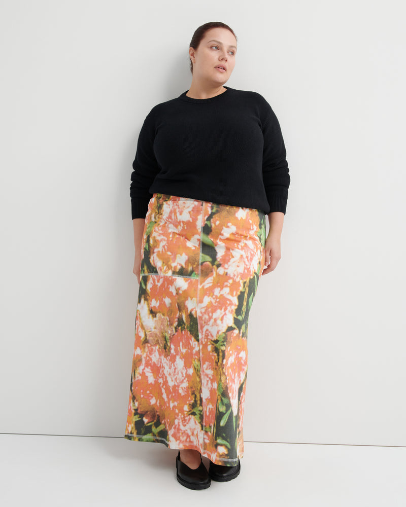 Woman wearing a black sweater and floral skirt against a white background