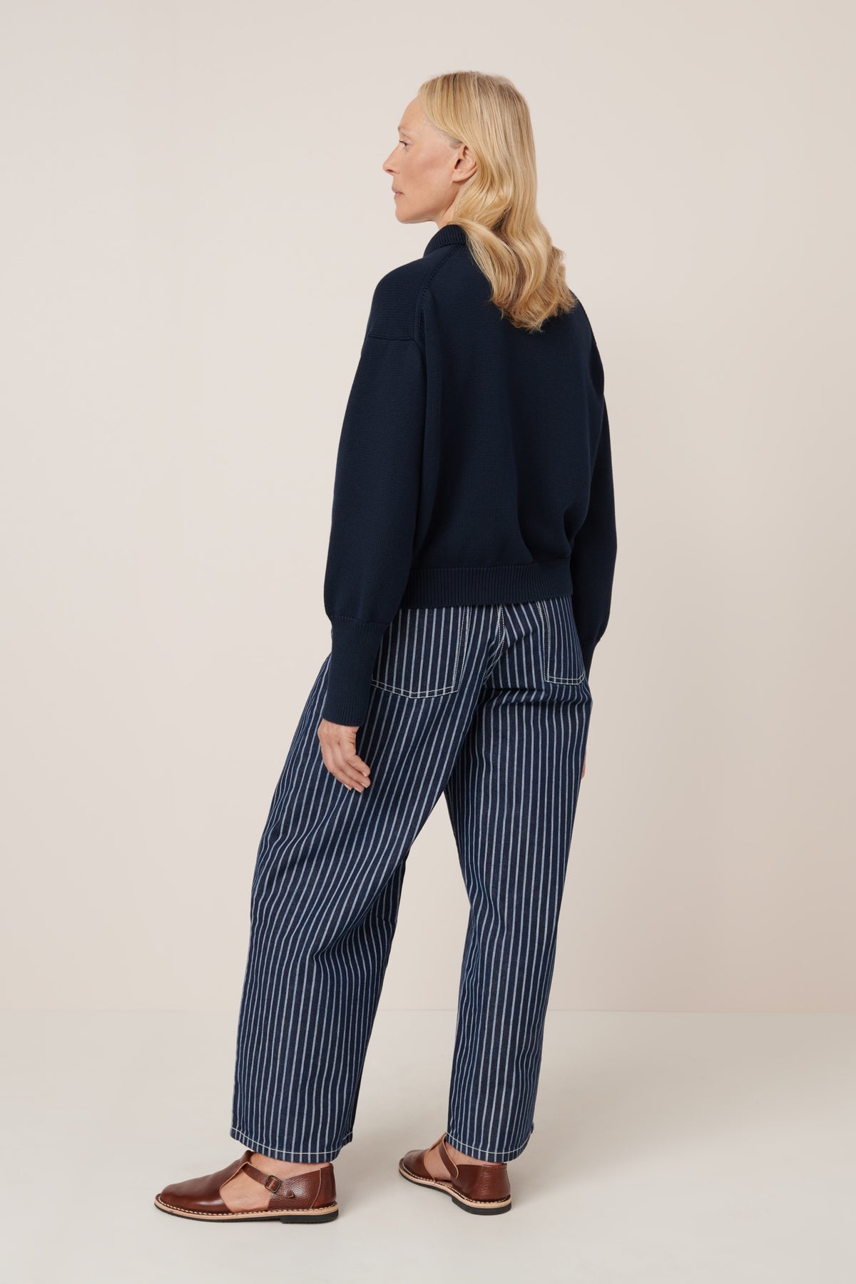Woman wearing a navy sweater and striped pants on a beige background