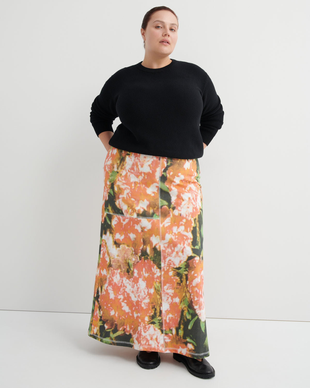 Person wearing a black sweater and floral skirt on a white background