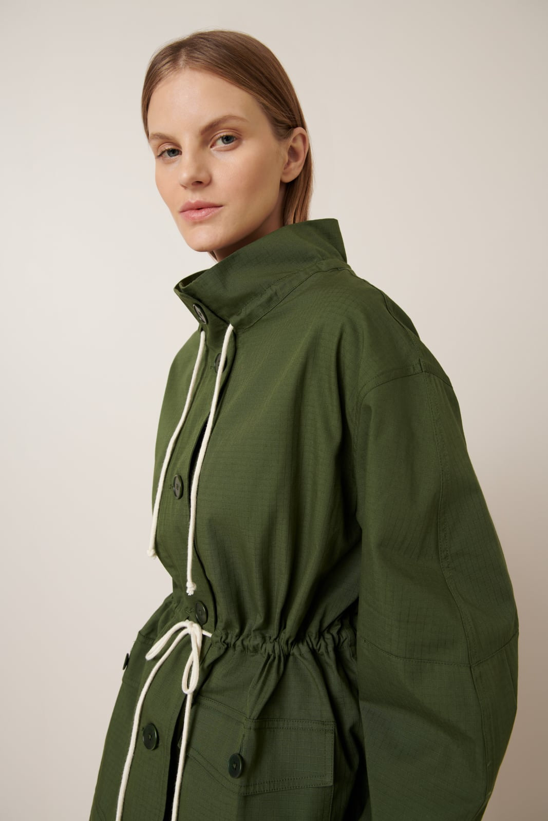 Woman wearing a green jacket with a white drawstring on a plain background