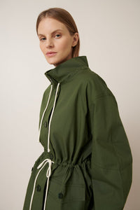 Woman wearing a green jacket with a white drawstring on a plain background