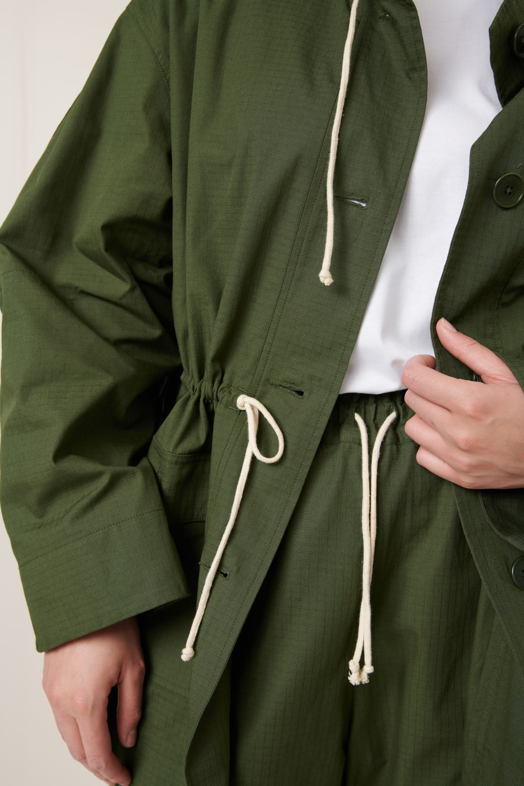 Green jacket with white drawstrings on a neutral background