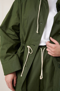 Green jacket with white drawstrings on a neutral background