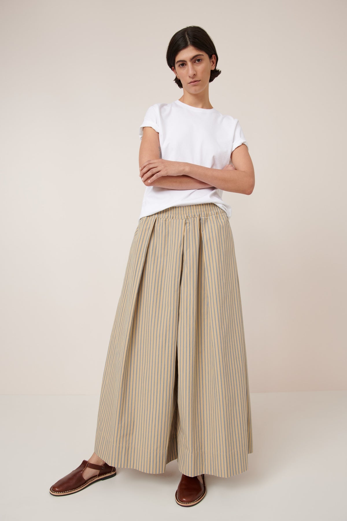 Person wearing a white t-shirt and beige striped wide-leg pants on a plain background