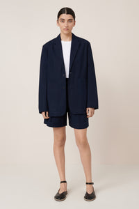 Person wearing a navy blazer and shorts set on a plain background