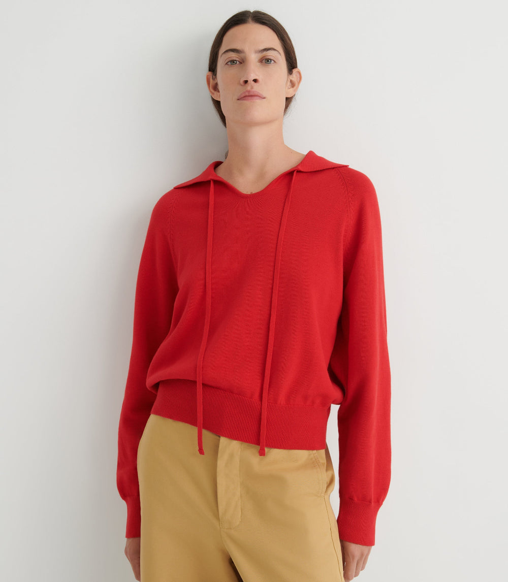 Person wearing a red collared sweater and tan pants against a white background