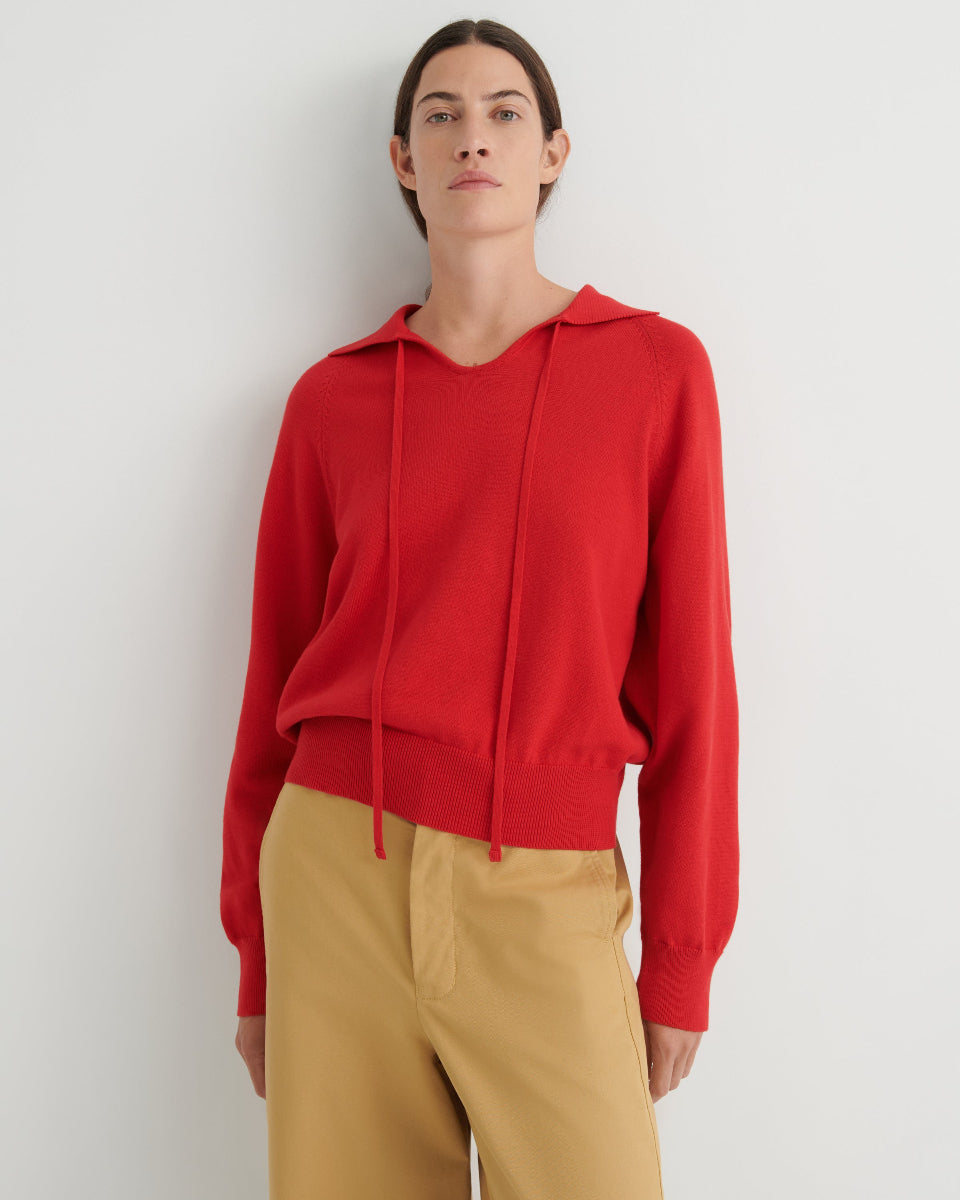 Person wearing a red collared sweater and tan pants on a white background