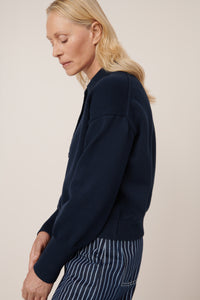 Woman wearing a navy sweater and striped pants against a beige background